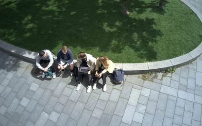 Four young people sitting on a low wall outside of ITU